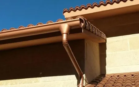 Canalón y bajante junto al alero de una vivienda con tejado de tejas